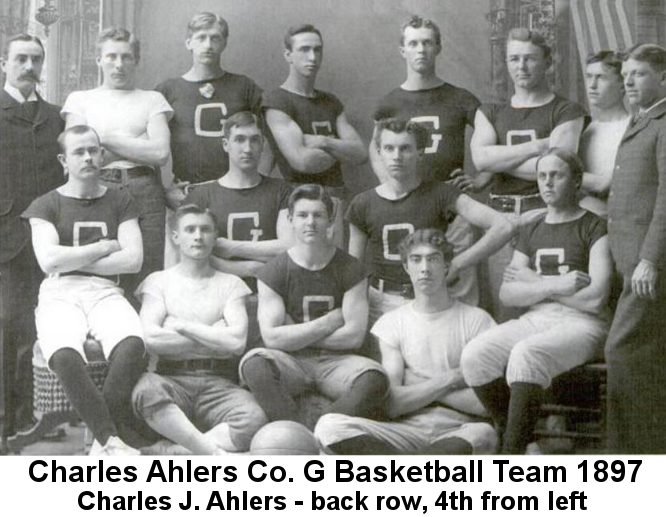 IMAGE/PHOTO: Charles Ahlers Company G Basketball Team 1897: Black and white photograph of several young men, most wearing black t-shirts with a large letter 'G' on them, standing or sitting in three rows. Charles Ahlers, with short black hair and muscular crossed arms, stands turned slightly to the left, 4th. from left in the back row.